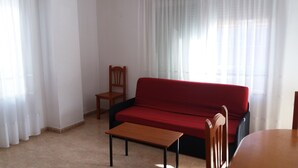 A living room with a red sofa, a wooden chair, and a small wooden table. - Apartamentos Oropesa sin Piscina 3000 (Oropesa del Mar)