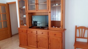 A wooden cabinet with glass doors containing cups and saucers, a television, and a chair. - Apartamentos Oropesa sin Piscina 3000 (Oropesa del Mar)