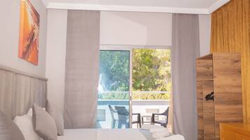 A modern hotel room with a large bed, a wooden wardrobe, a balcony with a table and chairs, and a painting on the wall.