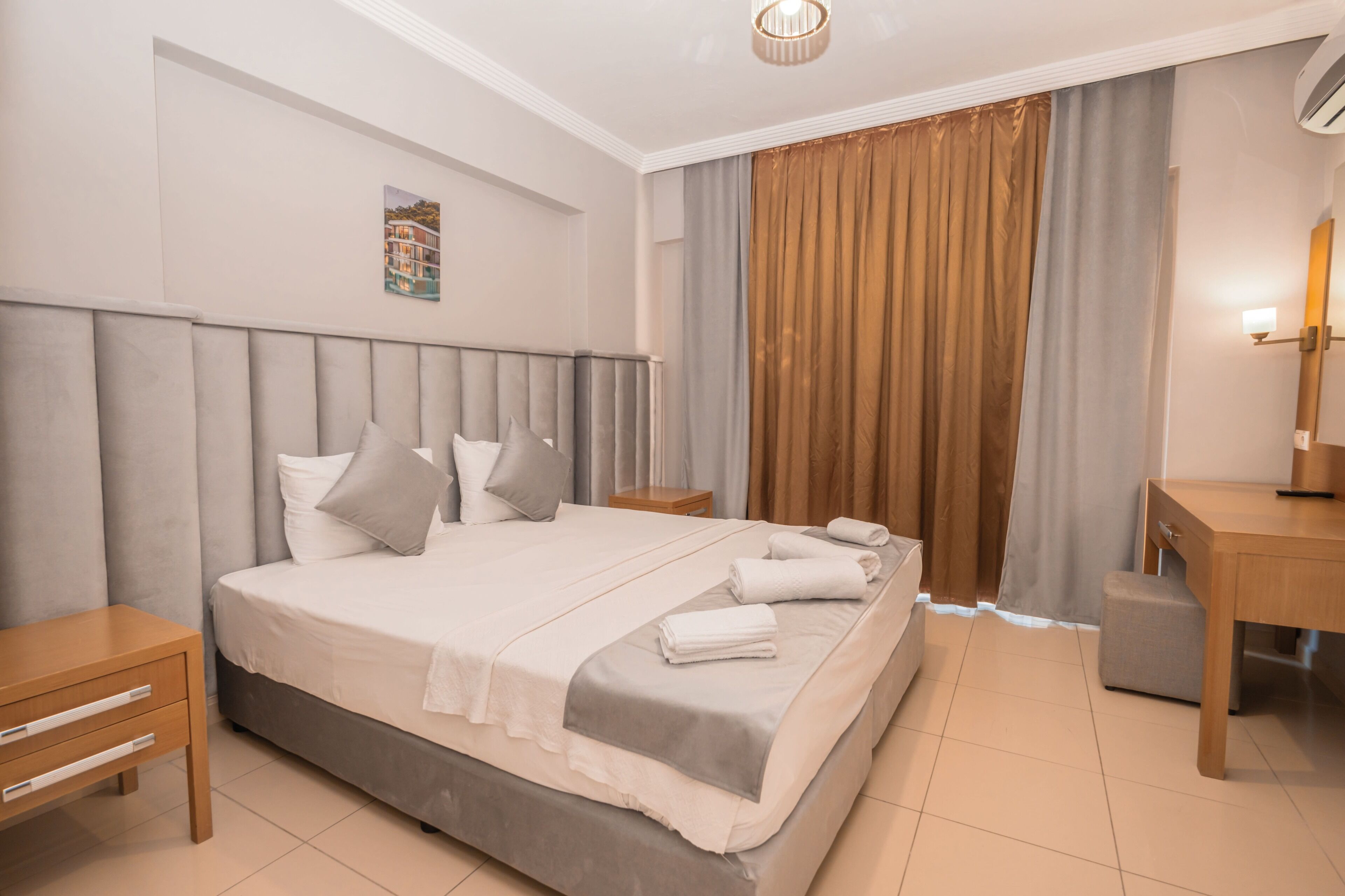 Una habitación de hotel ordenada con una cama grande, mesitas de noche, un escritorio y un espejo.