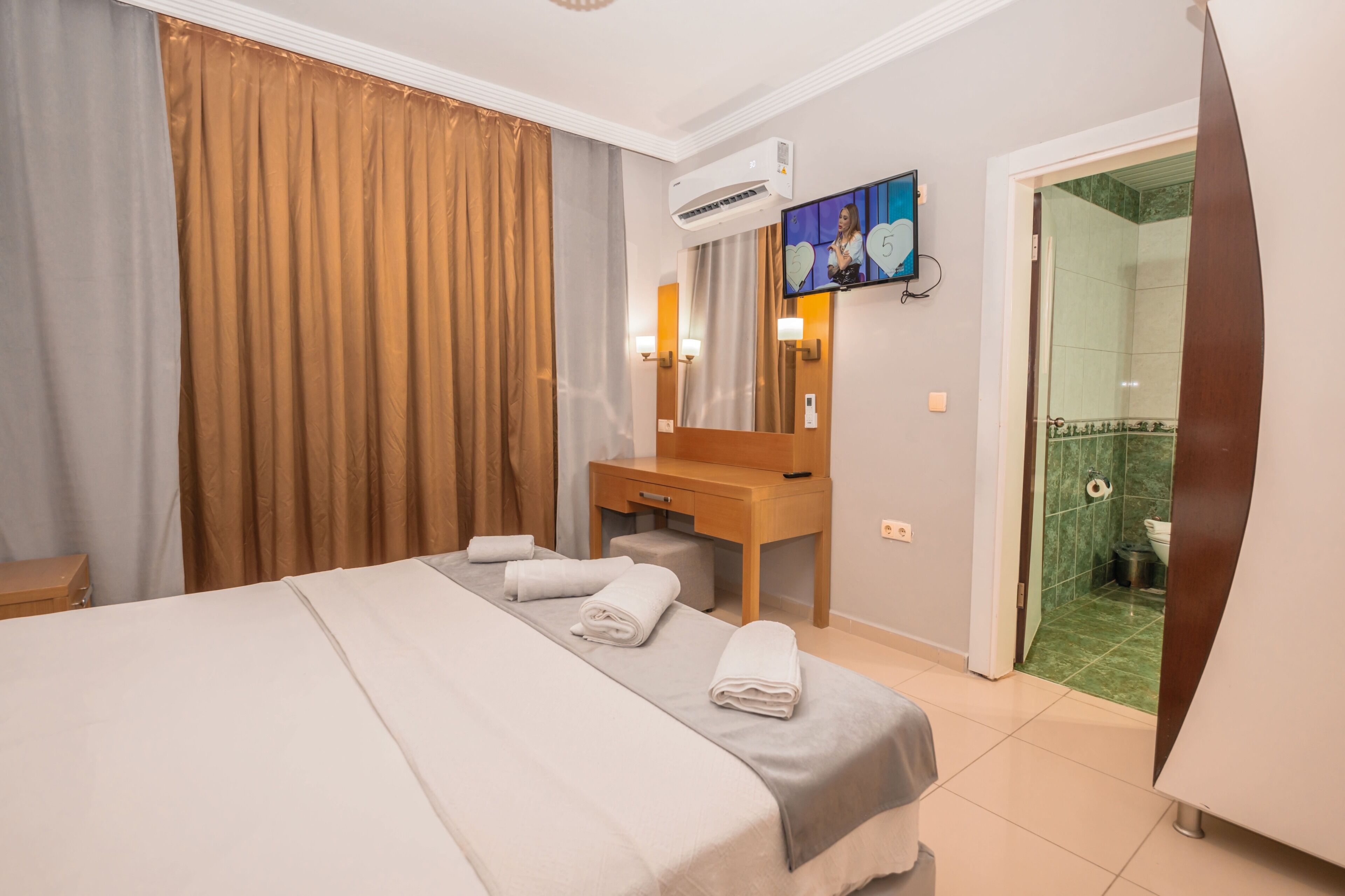 Habitación de hotel con una cama, un escritorio de madera, un televisor y un baño visible a través de una puerta abierta.