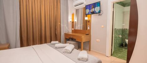 Habitación de hotel con una cama, un escritorio de madera, un televisor y un baño visible a través de una puerta abierta.