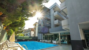 A modern outdoor swimming pool with lounge chairs and umbrellas, surrounded by buildings with balconies and large windows.