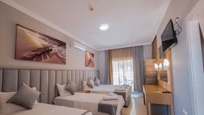 A hotel room with three beds, a TV, and artwork on the walls.