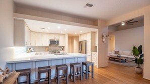 Une cuisine moderne avec des meubles blancs, un grand îlot central doté de tabourets, des appareils électroménagers en acier inoxydable et un plancher en bois.