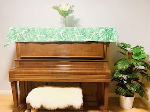 Un piano de madera con un otoman blanco y mullido, y una planta en maceta a su lado.