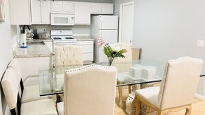 A modern kitchen with white cabinetry, a glass dining table, and cream-colored chairs.