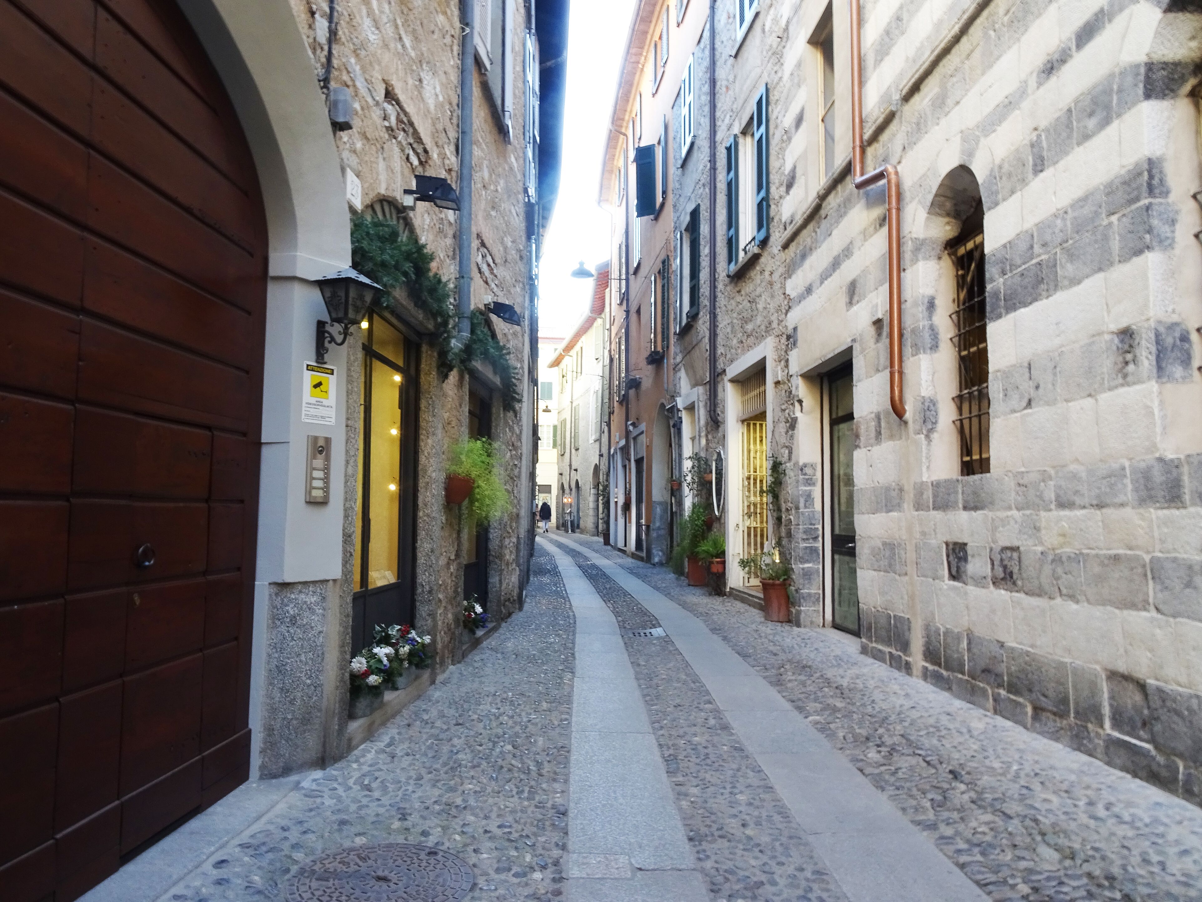 A narrow cobblestone street flanked by historic stone buildings with arched doorways and windows.