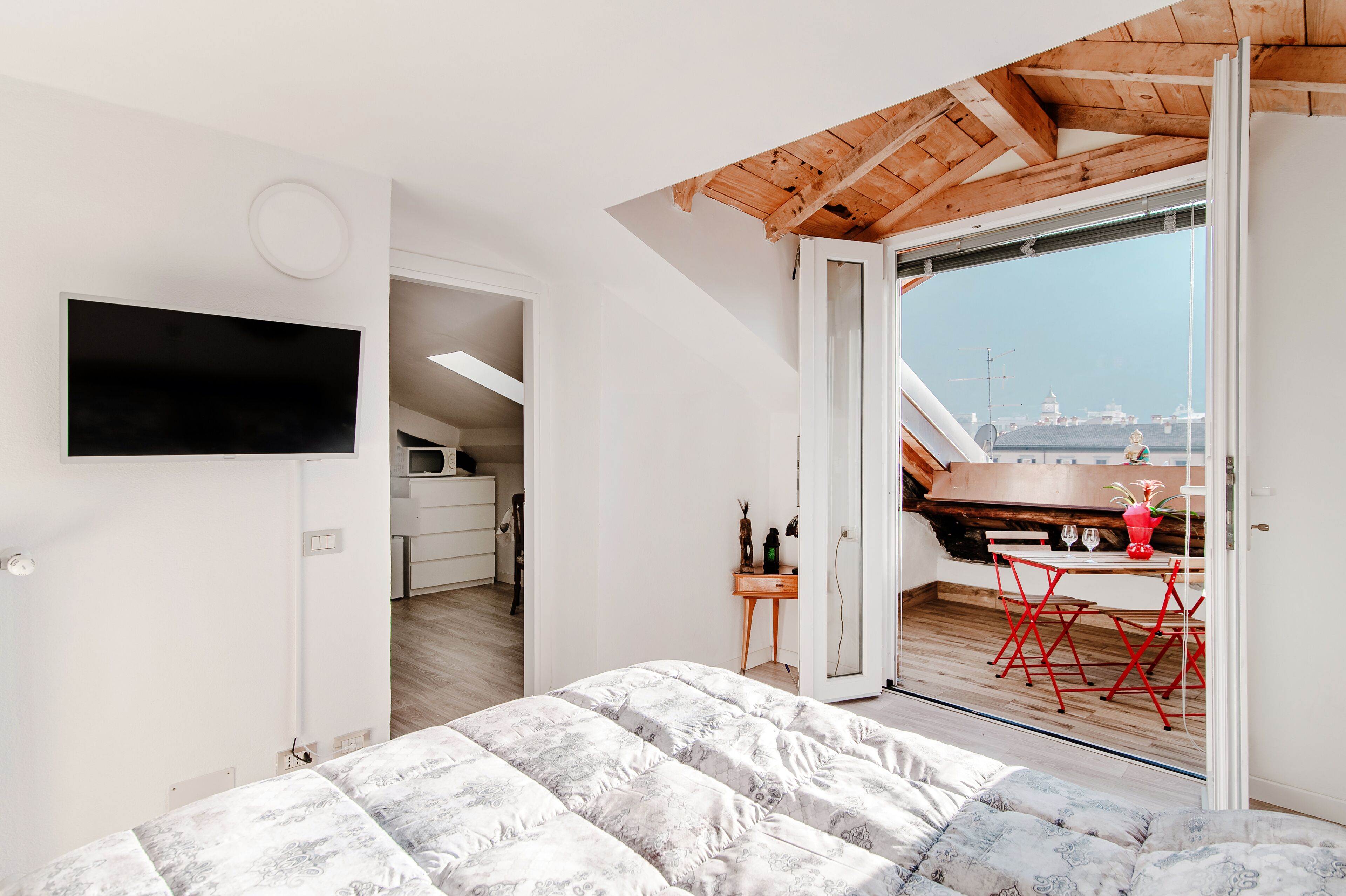 A bedroom with a bed, a TV mounted on the wall, and a balcony with a view of the sea.