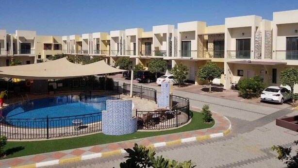 A modern residential building with a swimming pool, outdoor seating, and a covered area.