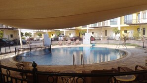 A circular swimming pool with a surrounding fence, lounge chairs, and a covered seating area.