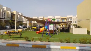 A playground with slides and swings, surrounded by a well-maintained lawn and a building with balconies.