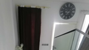 A modern bathroom with a glass shower enclosure, a dark curtain, and a wall-mounted clock.
