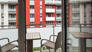A balcony with wicker chairs and a small table, overlooking a building with red and white exterior walls. - Brasov Holiday Apartments-purple (Brasov)