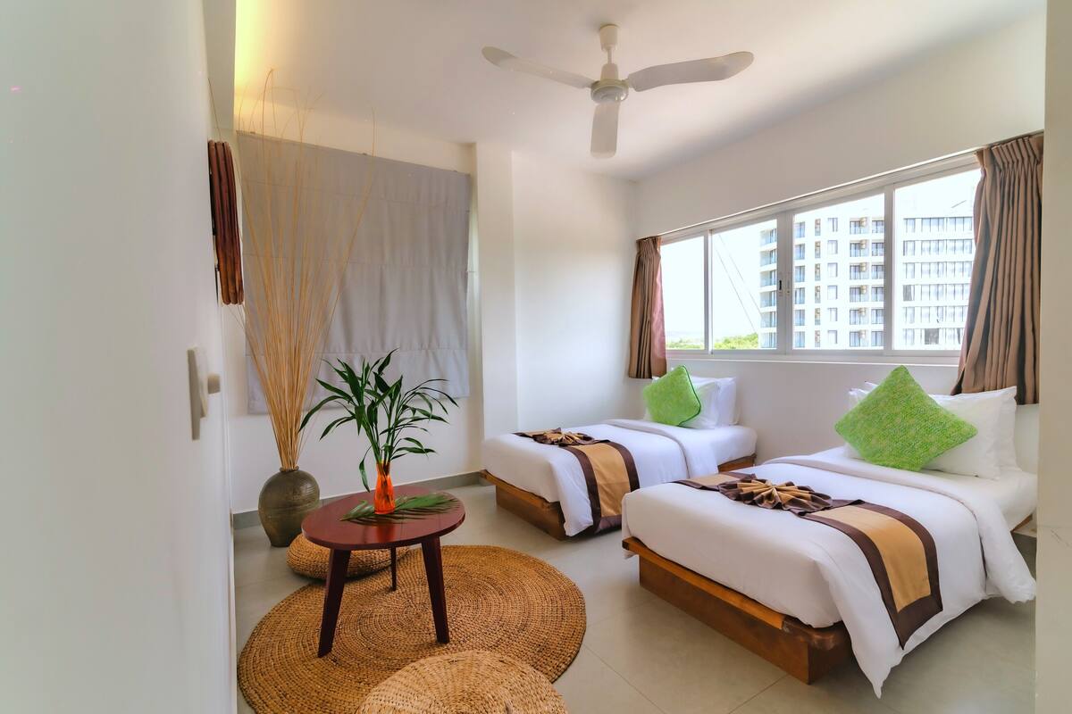 A hotel room with two beds, a ceiling fan, a large window, and a view of a building outside.