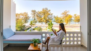 Ein Balkon mit Blick auf Bäume und eine Straße, ein weißes Sofa, ein Tisch mit einer Pflanze und eine Person, die ein Buch liest.