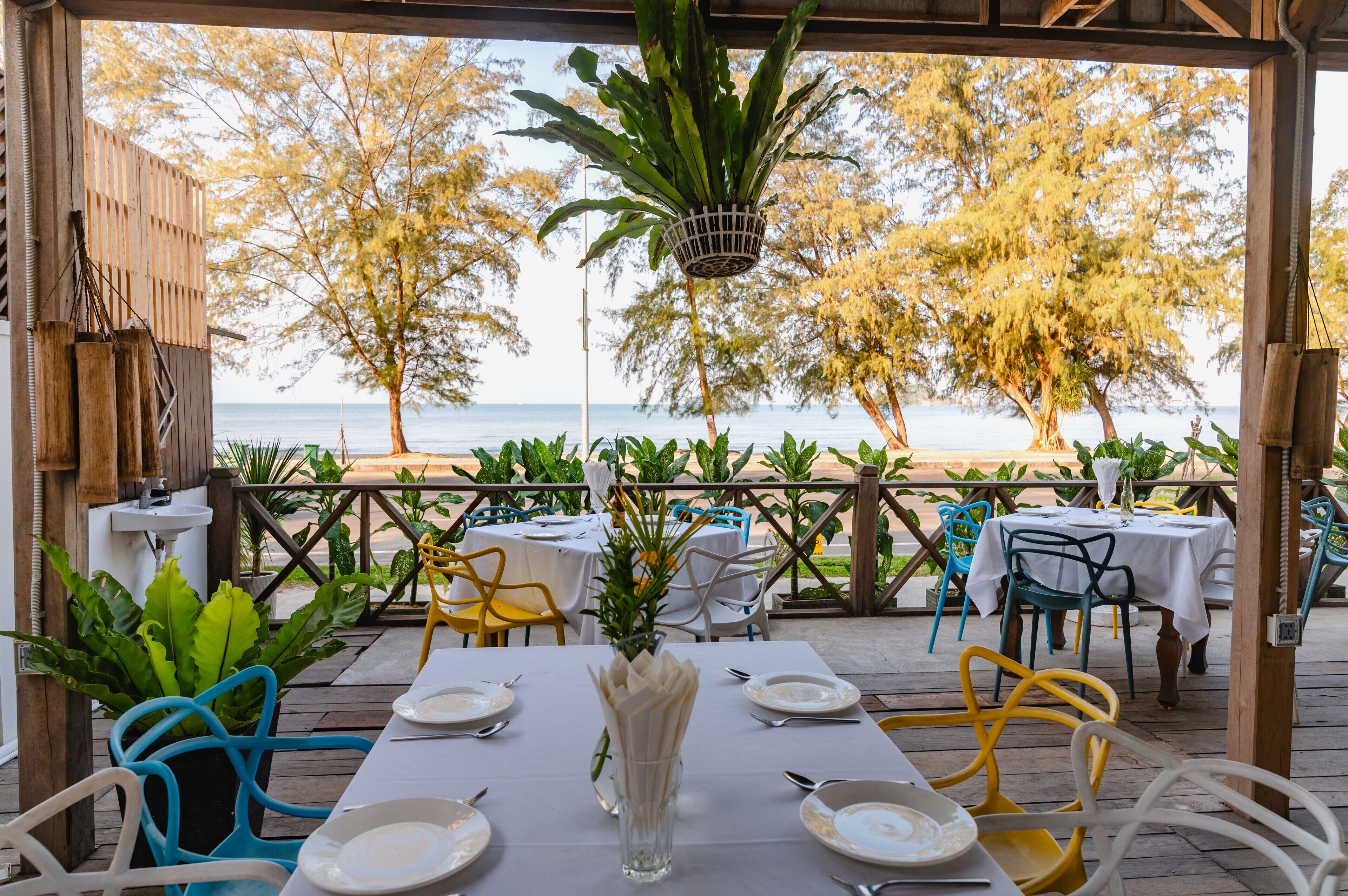 A covered outdoor dining area with tables and chairs, overlooking a beach.