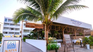 Eingangsbereich eines Resorts mit einer Palme, einem Schild für Naiya Sea Resort und Außenmöbeln.
