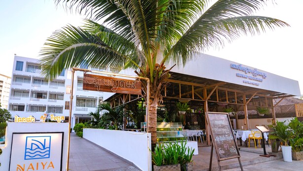 A resort entrance with a palm tree, a sign for Naiya Sea Resort, and outdoor seating. - Naiya Sea Resort (Sihanoukville)