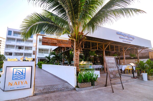 Eingangsbereich eines Resorts mit einer Palme, einem Schild für Naiya Sea Resort und Außenmöbeln.