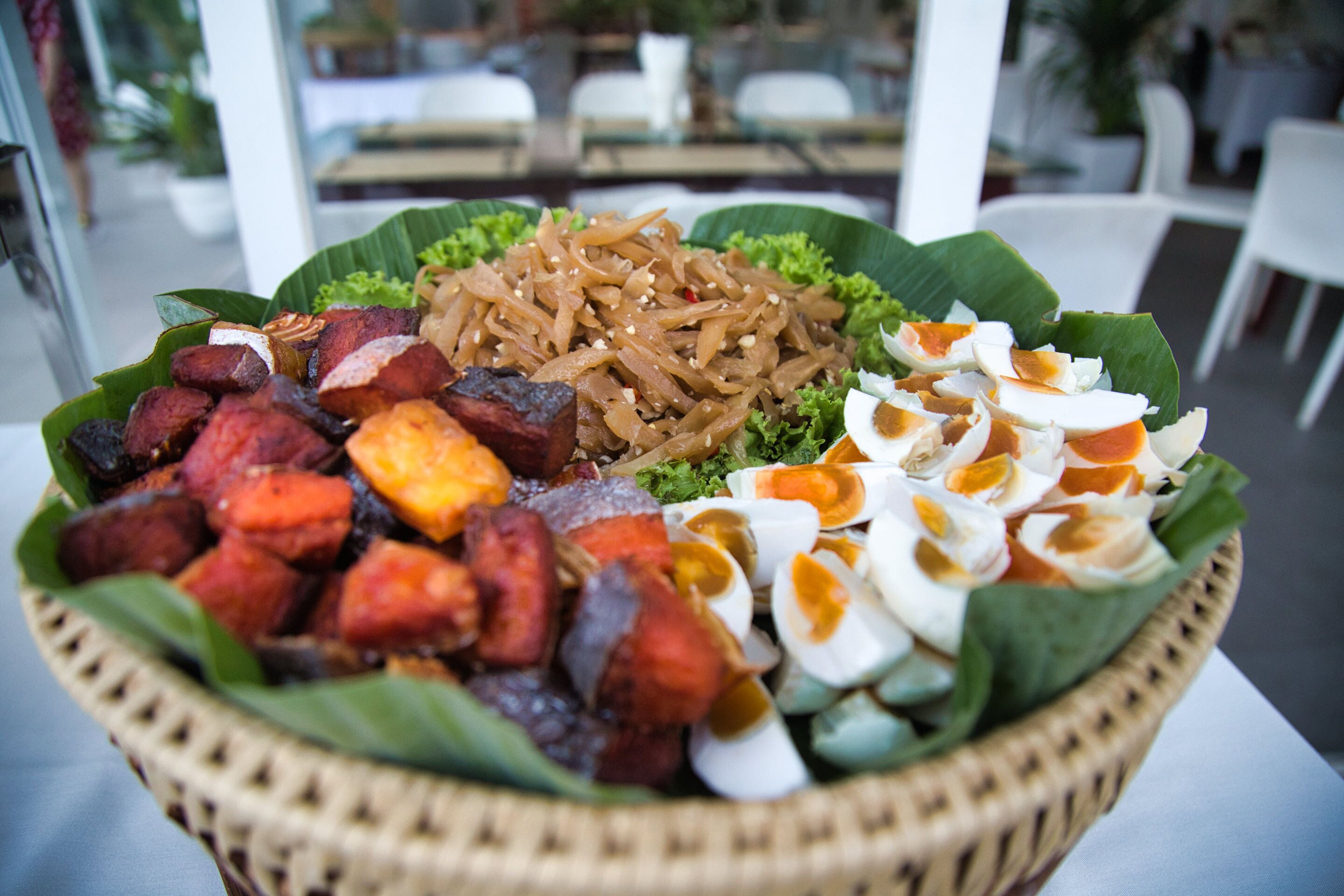 A food platter with various dishes including noodles, meat, and boiled eggs, served on a banana leaf.