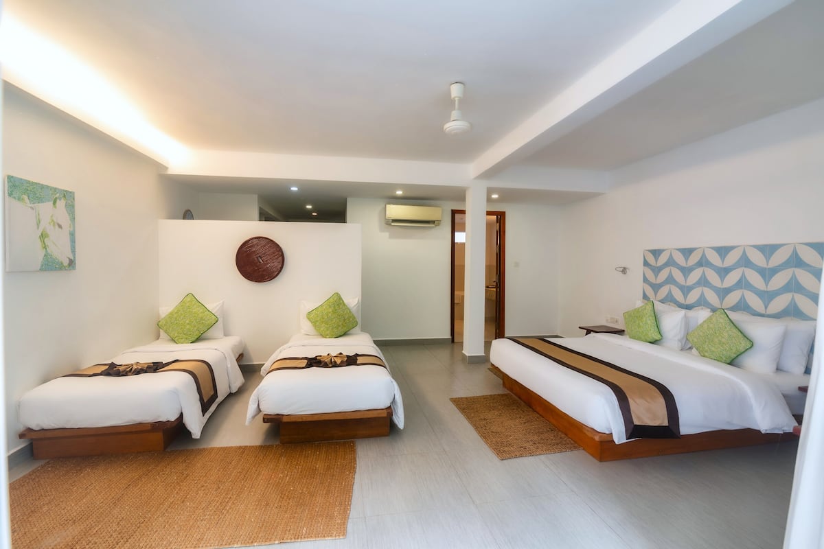 A hotel room with two single beds, a larger bed, and a small table.