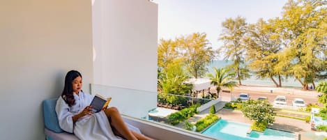 A person reclining on a balcony with a book, overlooking a pool and outdoor seating area.