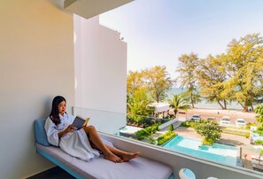 Une personne est allongée sur un balcon, un livre à la main, et elle a une vue sur une piscine et un espace de détente extérieur.