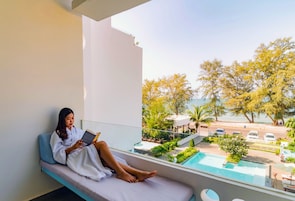 A person reclining on a balcony with a book, overlooking a pool and outdoor seating area.