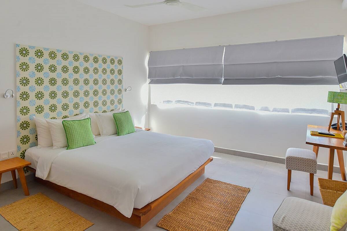 A bedroom with a bed, a bedside table, a chair, a desk, a lamp, and a window with a view.