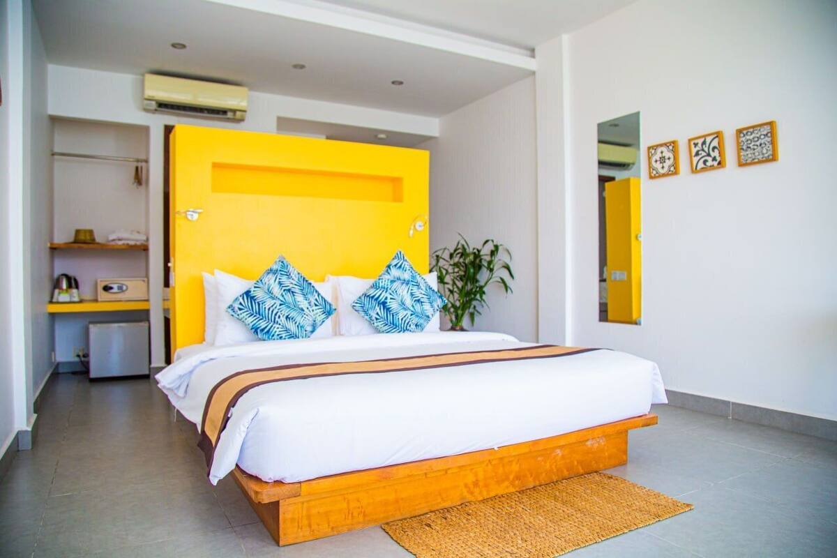 A modern hotel room with a wooden bed, white bedding, and a yellow accent wall.