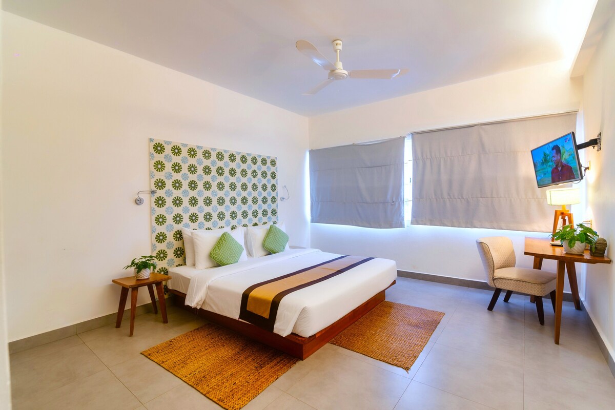 A hotel room with a bed, a desk, a chair, a television, and a ceiling fan.