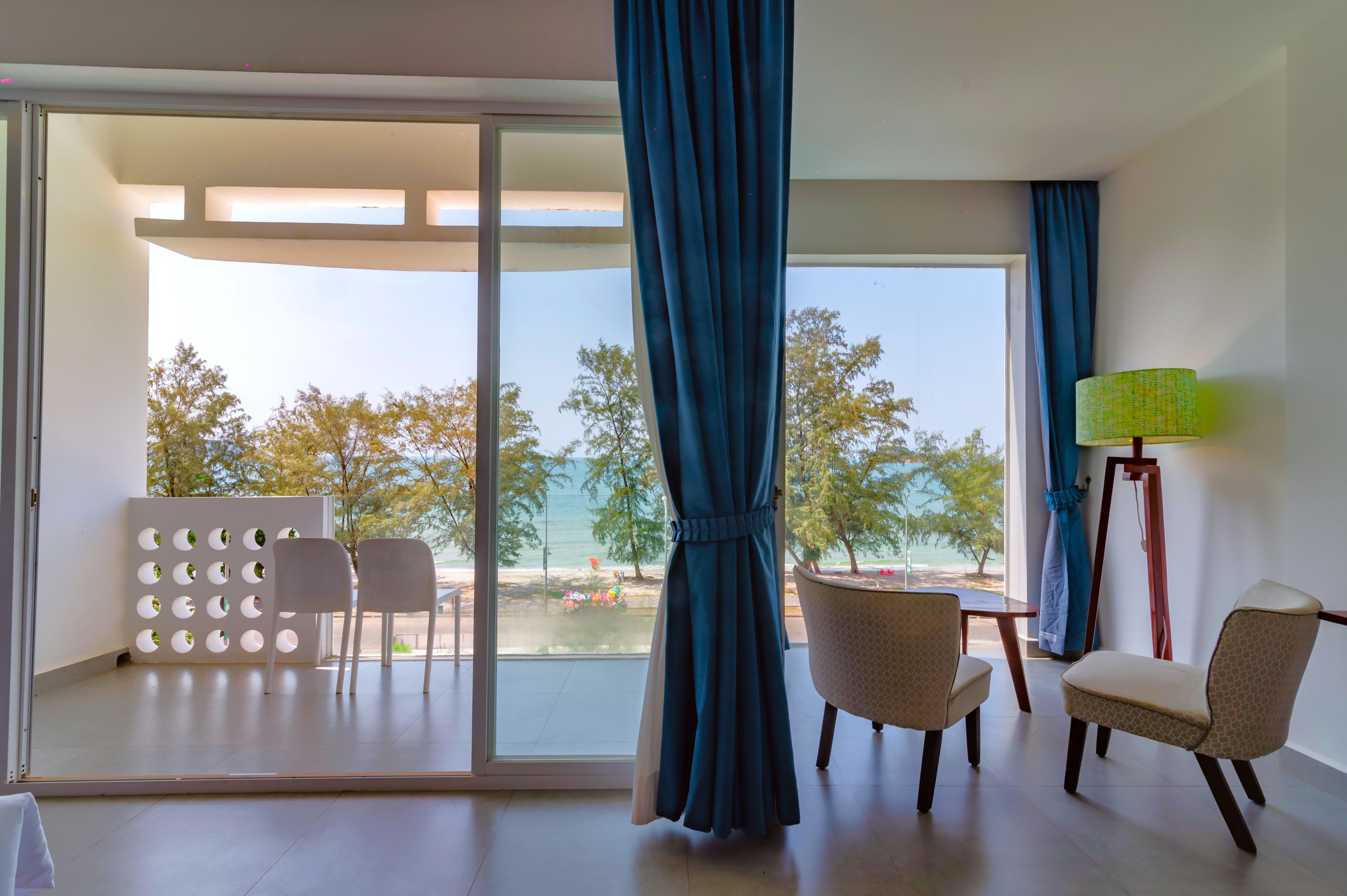 Een kamer met uitzicht op het strand, twee stoelen, een tafel en een lamp.