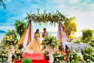 A beach wedding ceremony with floral decorations and a red carpet.