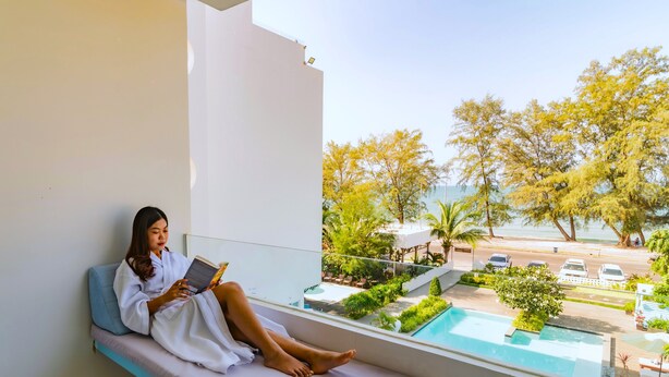 Eine Person sitzt auf einem Balkon mit Blick auf ein Schwimmbecken und Grünflächen.