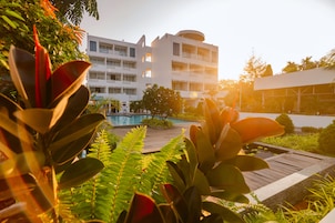 Un hotel moderno con piscina, rodeado de exuberante vegetación y un cielo despejado.