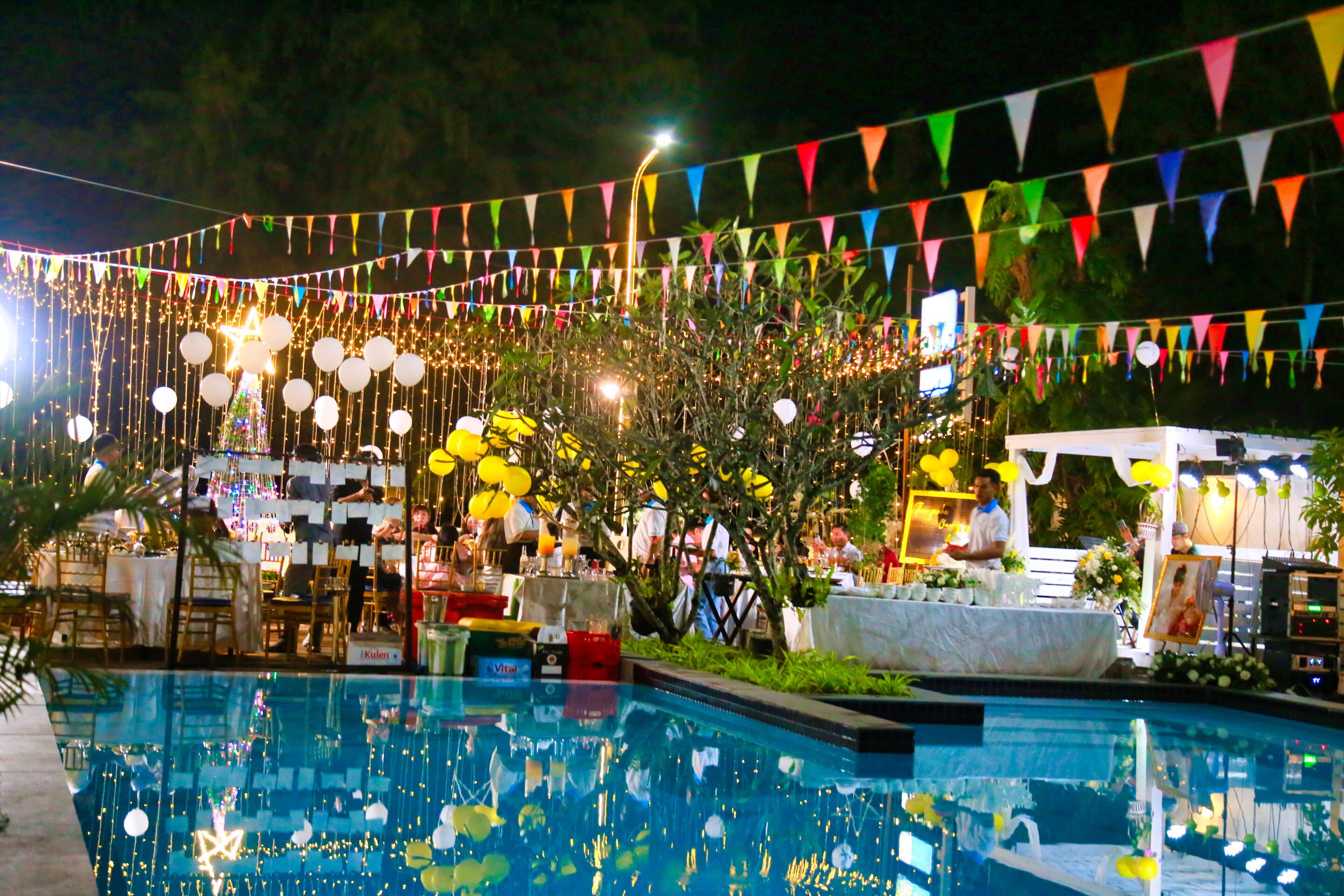 Un área de piscina con un bar y asientos, rodeada de llamativas banderas triangulares y luces de adorno.