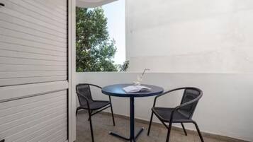 Un balcón con una mesa redonda y dos sillas, una pared blanca y un árbol al fondo.
