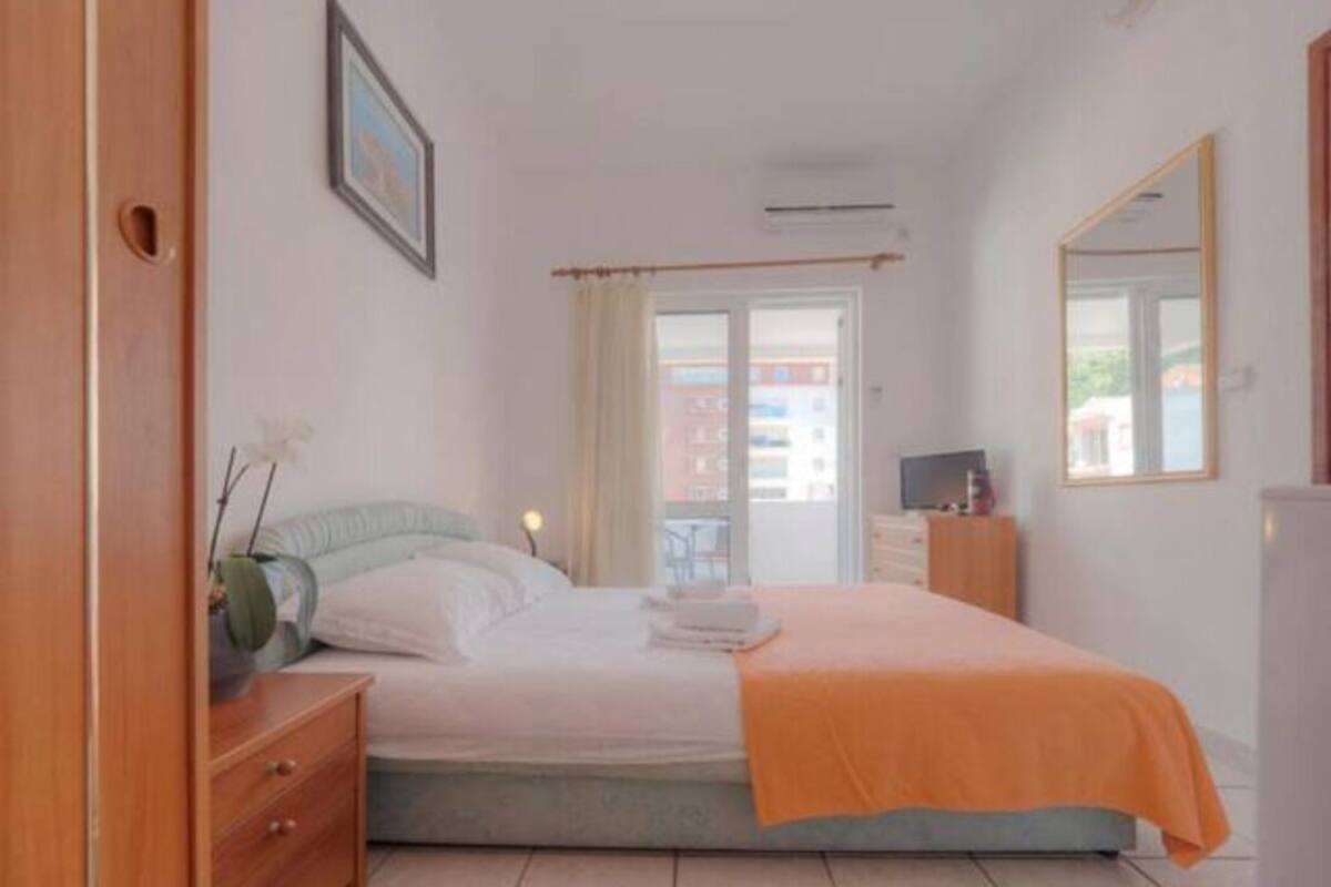A bedroom with a bed, a dresser, a television, and a window with curtains.