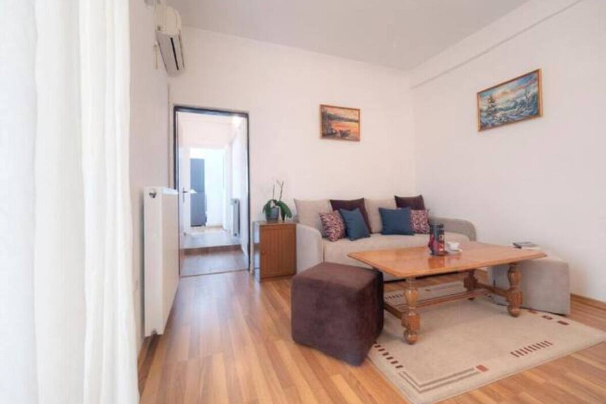 A modern living room with a wooden floor, a sofa set, a coffee table, and two paintings on the wall.