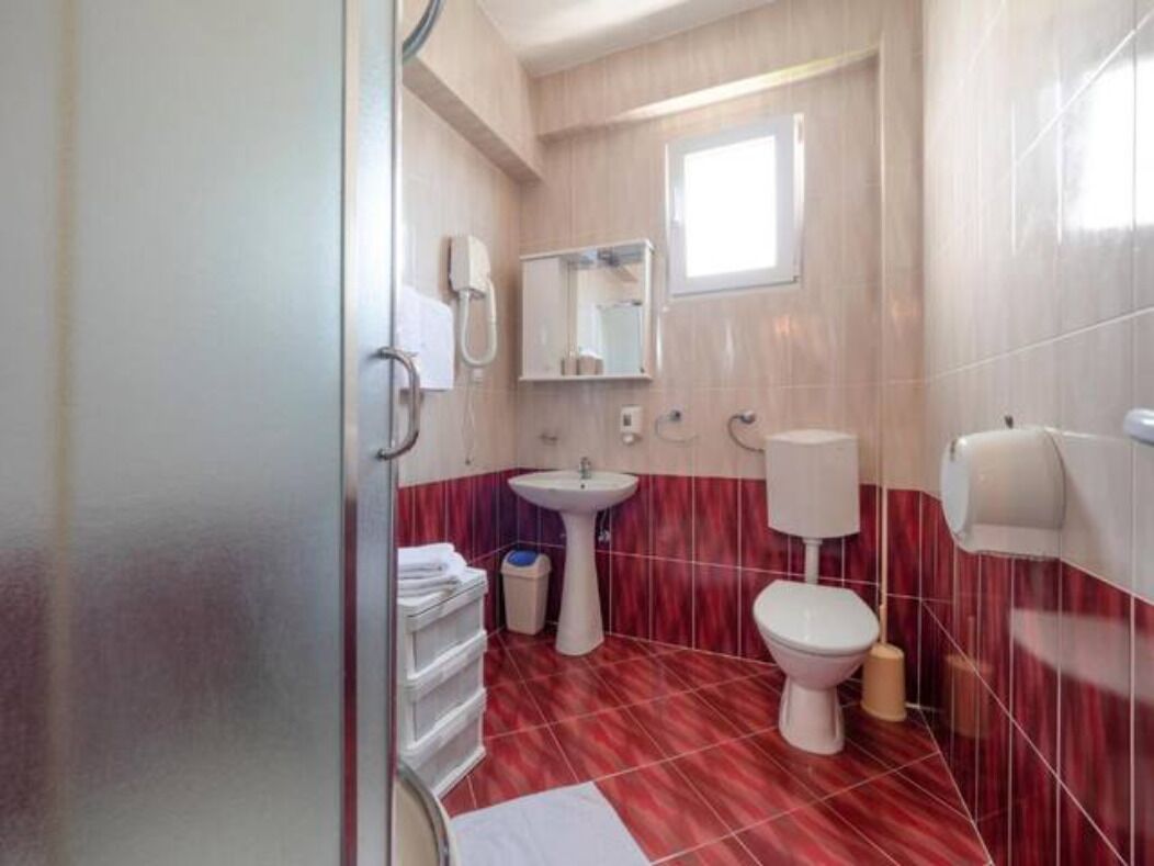 Een badkamer met een rode betegelde vloer, een witte wastafel, een toilet en een spiegel.