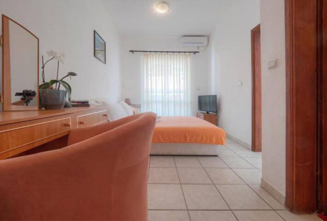 A hotel room with a bed, a desk with a computer, a mirror, and a potted plant.