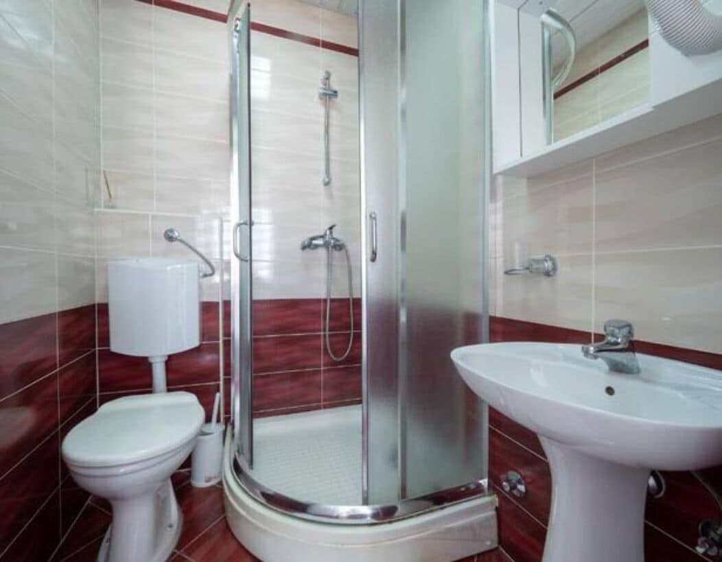 A bathroom with a glass-enclosed shower, a toilet, and a sink.