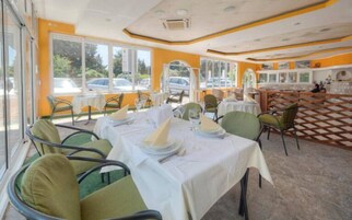 Ein Restaurant mit Außenbereich, Tische mit weißen Tischdecken und grüne Stühle, sowie ein Schachbrettmuster auf dem Boden.