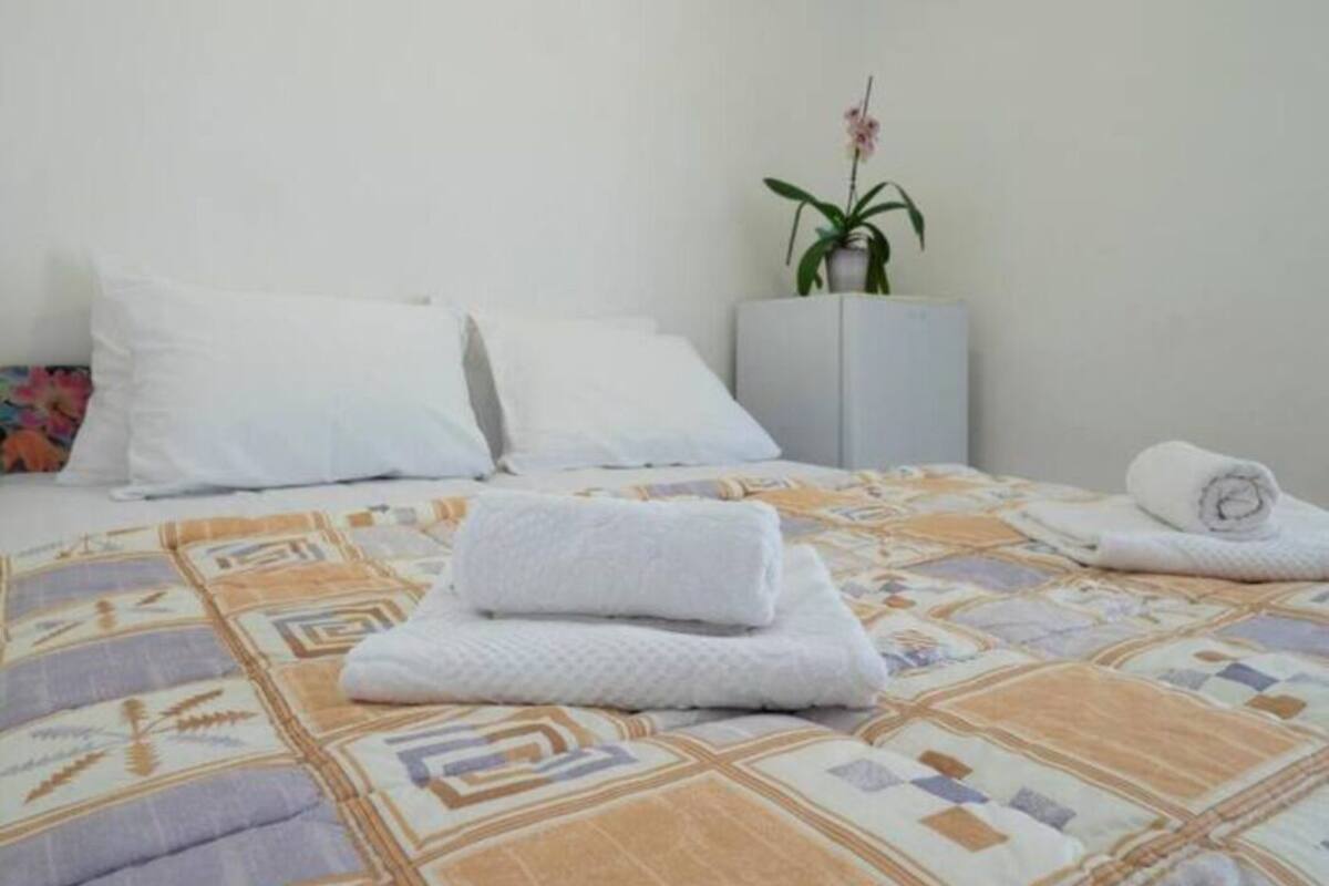 A neatly made bed with a patterned bedspread, two white pillows, and a rolled towel on the bed.
