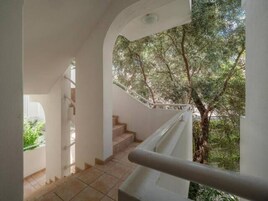 Eine Treppe mit Glasgeländer führt zu einem Balkon mit Blick auf Bäume.