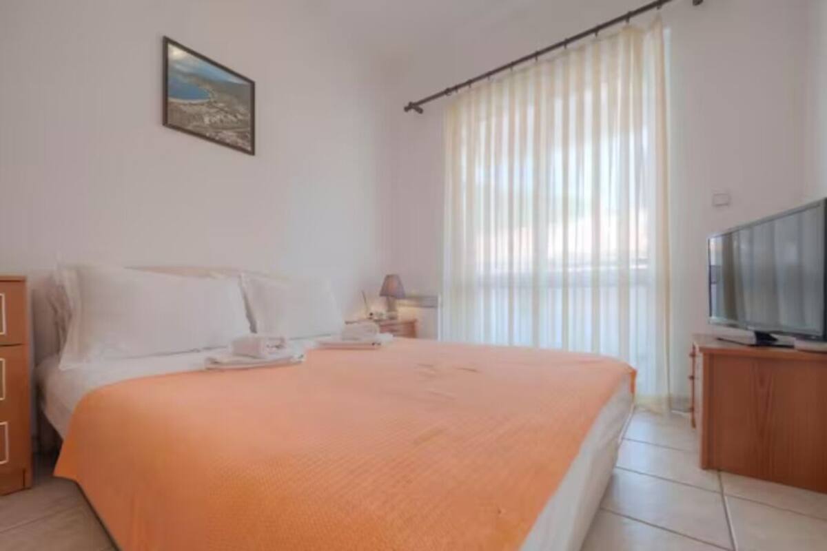 A bedroom with a bed, a television, a nightstand, and a window with curtains.