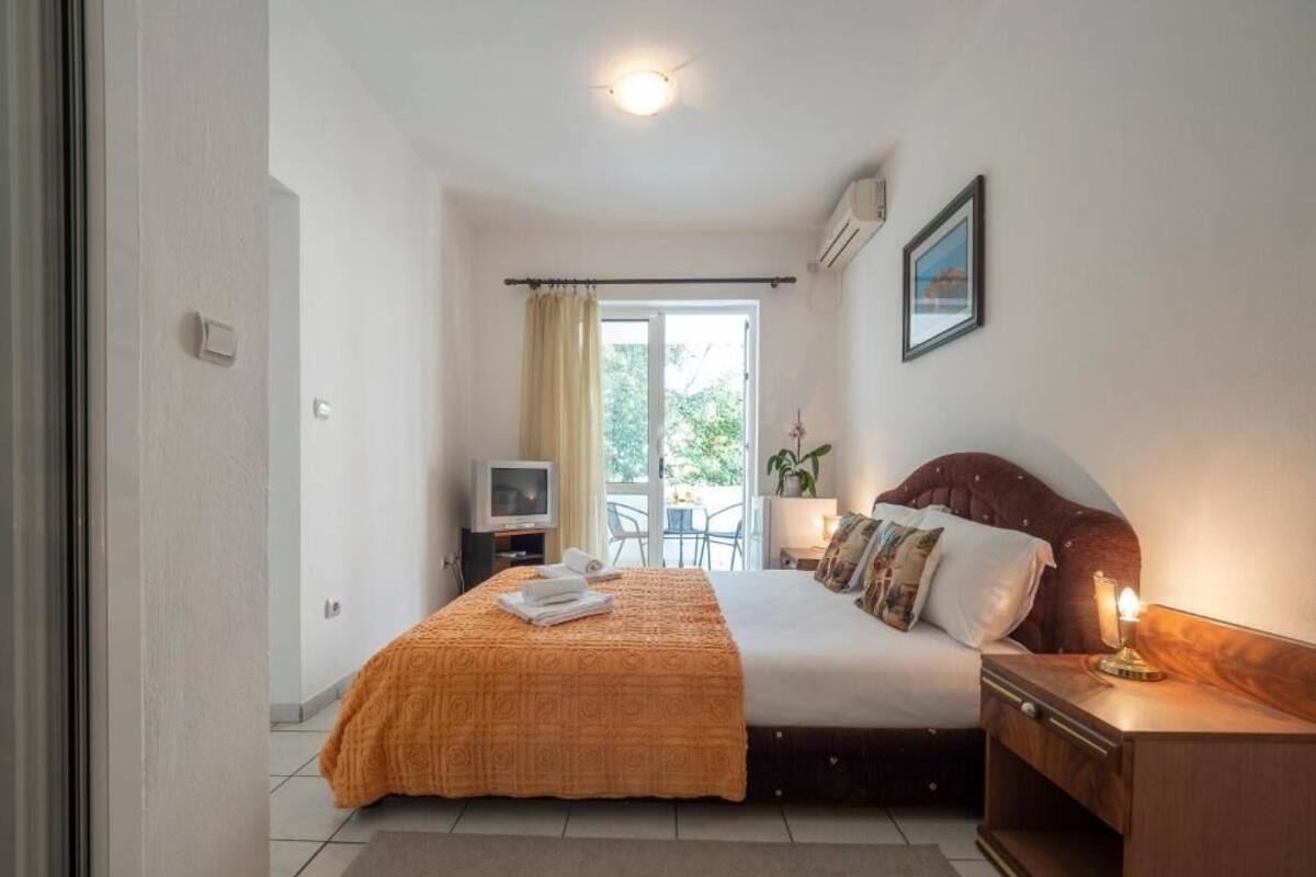 A bedroom with a bed, bedside table, TV, and a view of the outdoors.