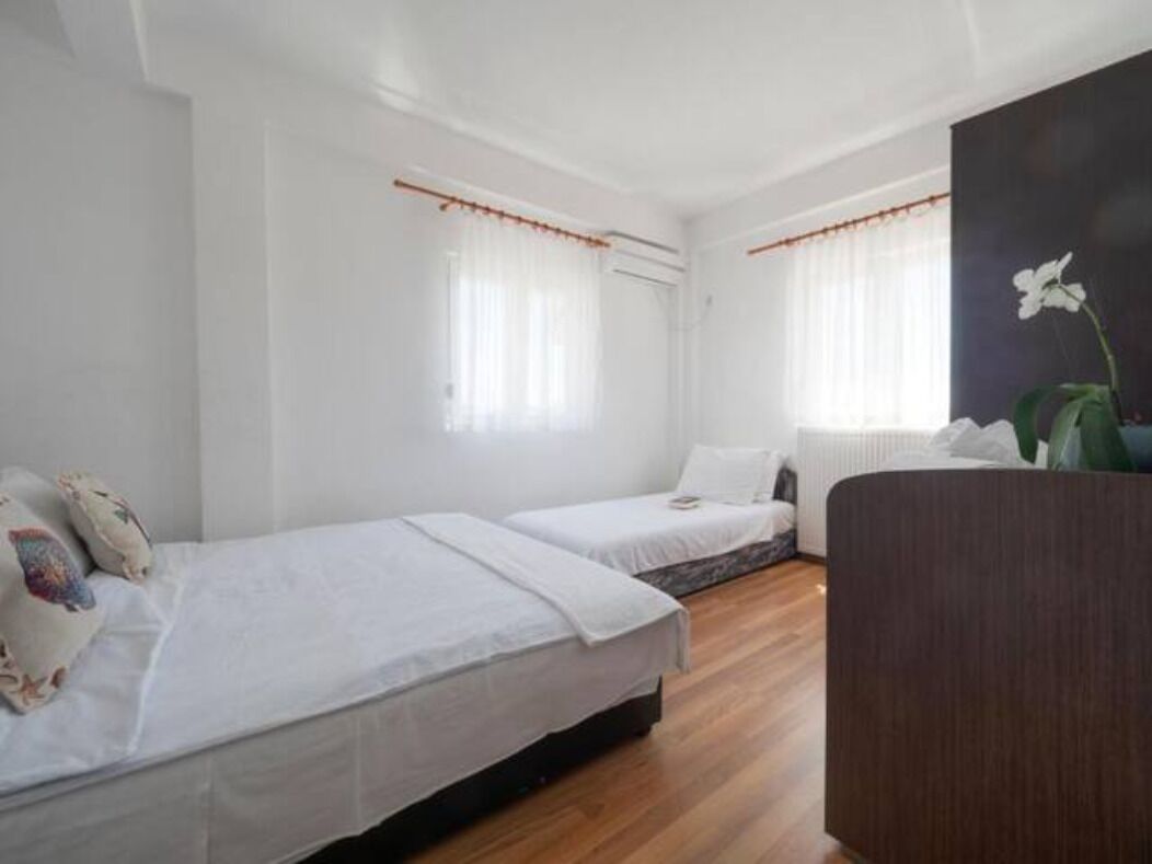 Een kamer met twee eenpersoonsbedden, witte beddengoed en een groot raam met gordijnen.
