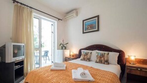 A hotel room with a large bed, a television, a desk, and a balcony with curtains.